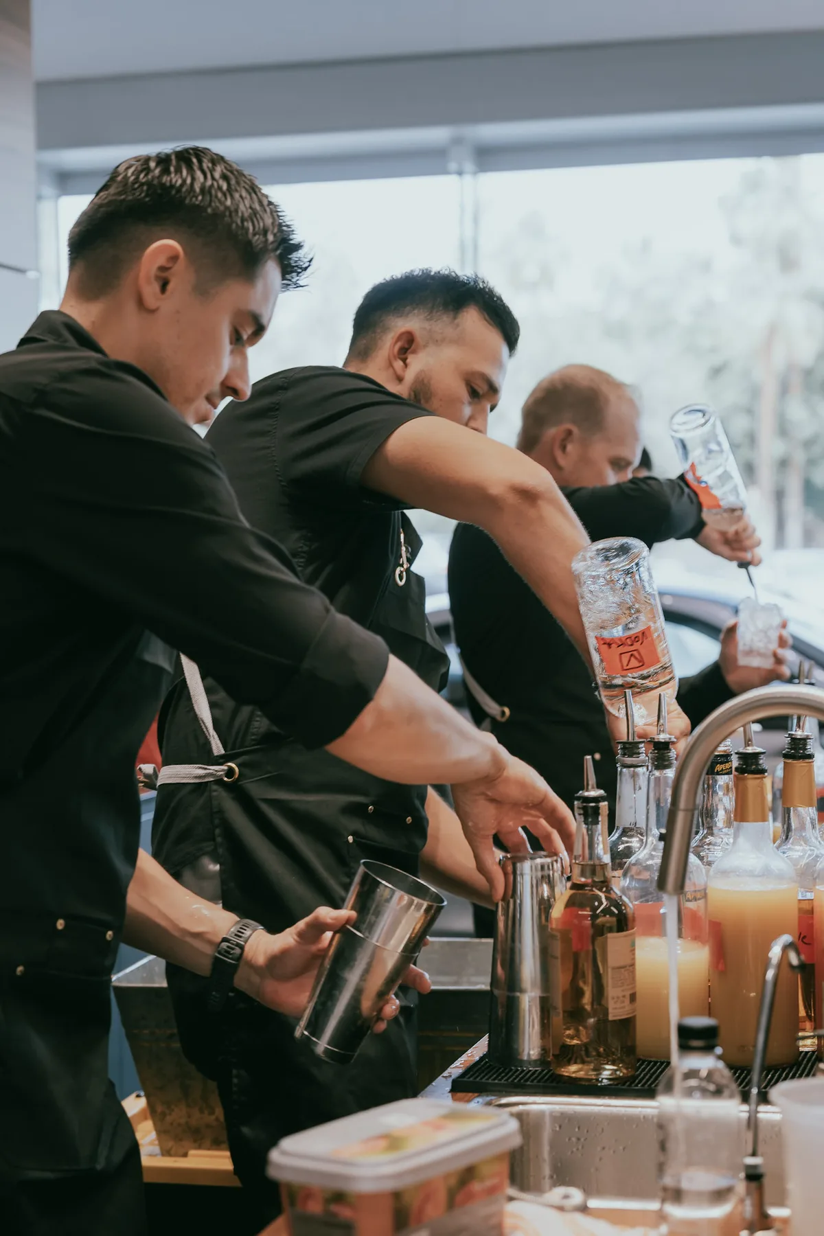 Three That’s The Spirit bartenders working side by side at a busy indoor event bar