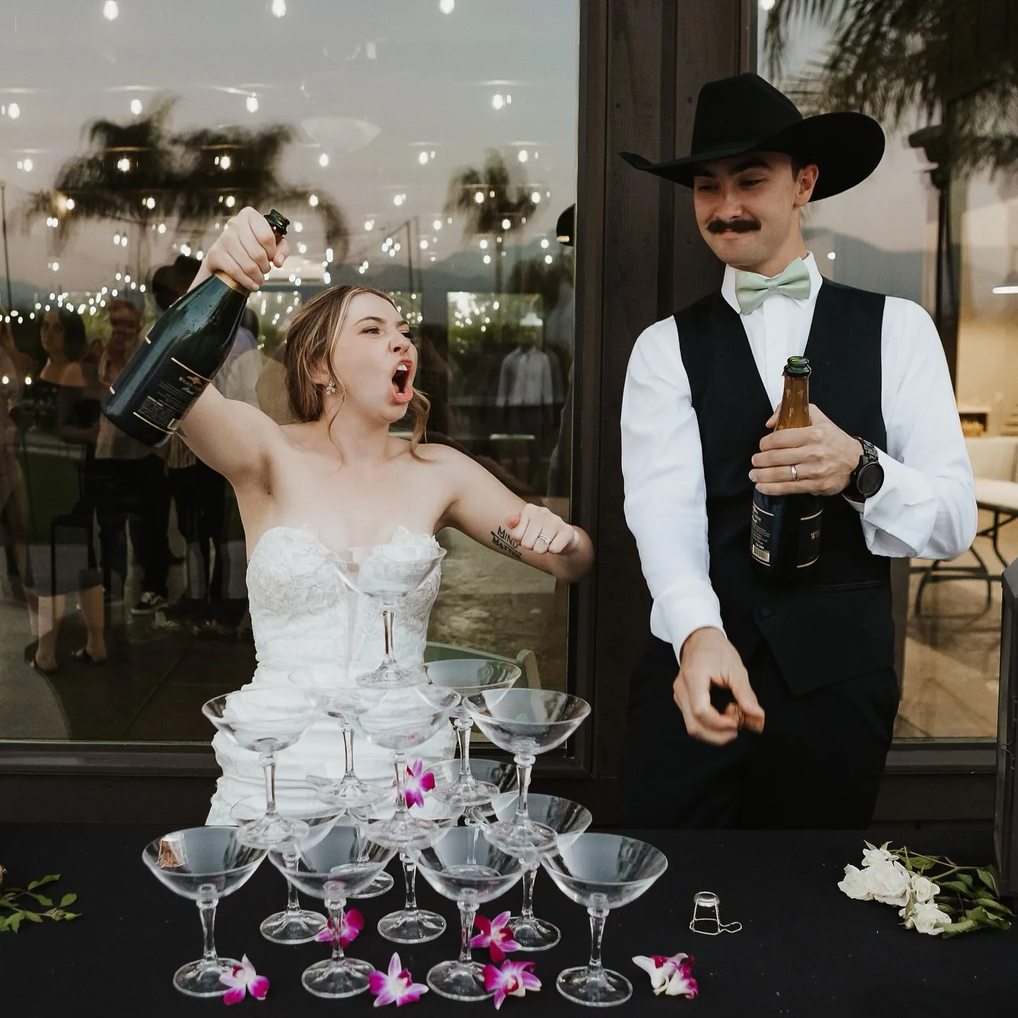 Bride cheering as the groom pours champagne over their reception tower