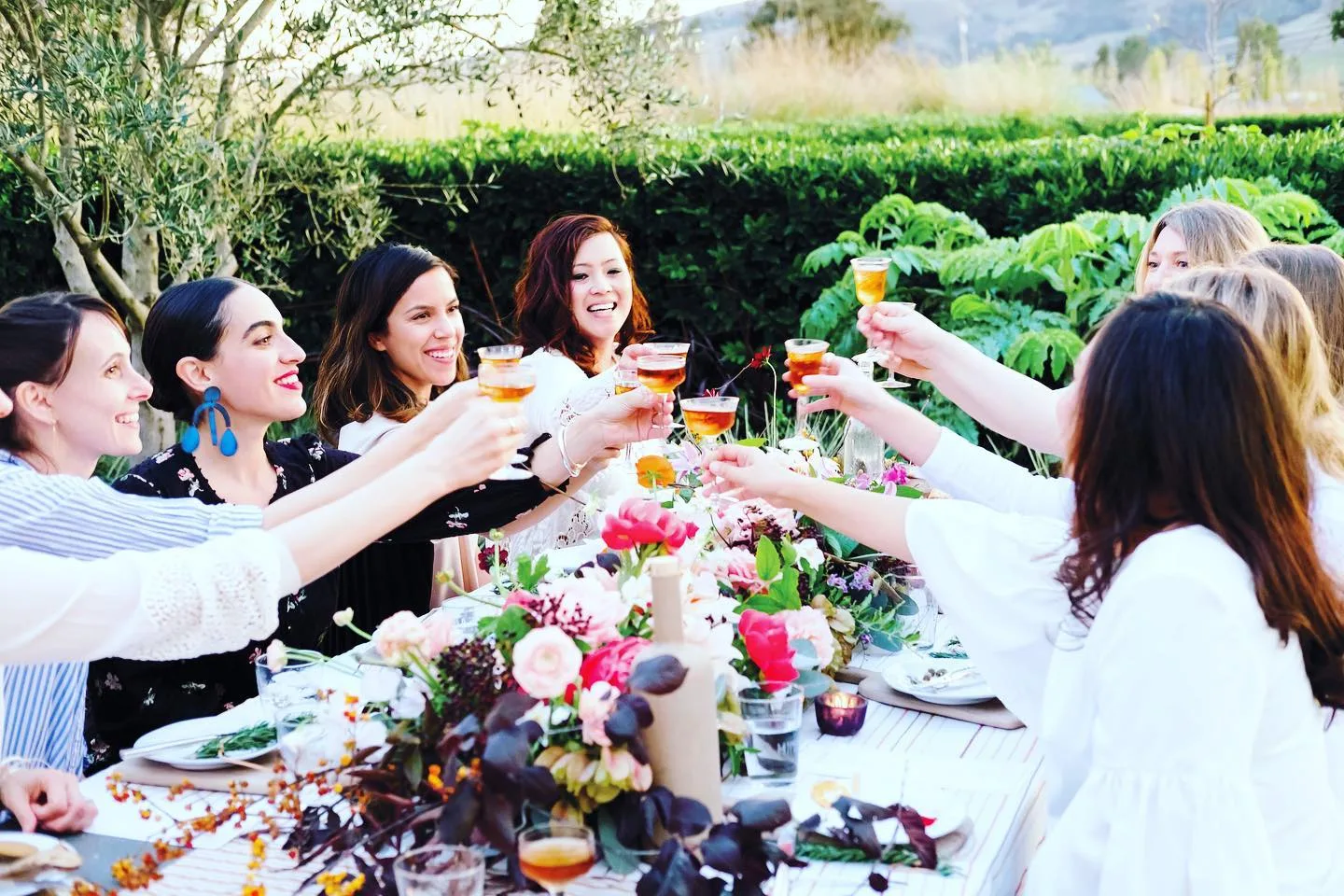 Guests raising cocktails around a flower-filled outdoor table with desert mountains in the distance