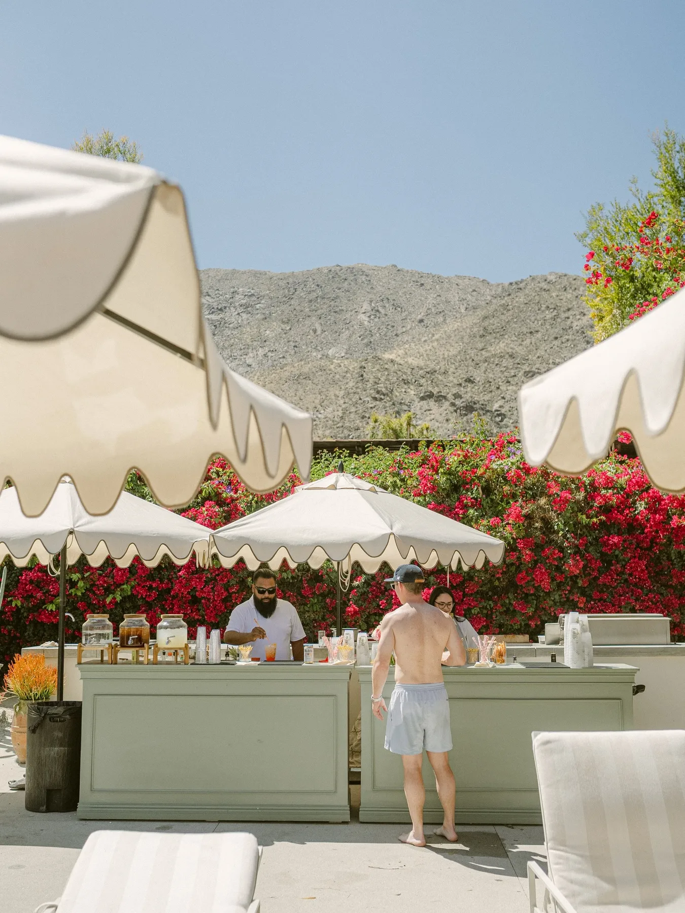Outdoor cocktail bar beneath white umbrellas with bougainvillea and the San Jacinto Mountains behind it