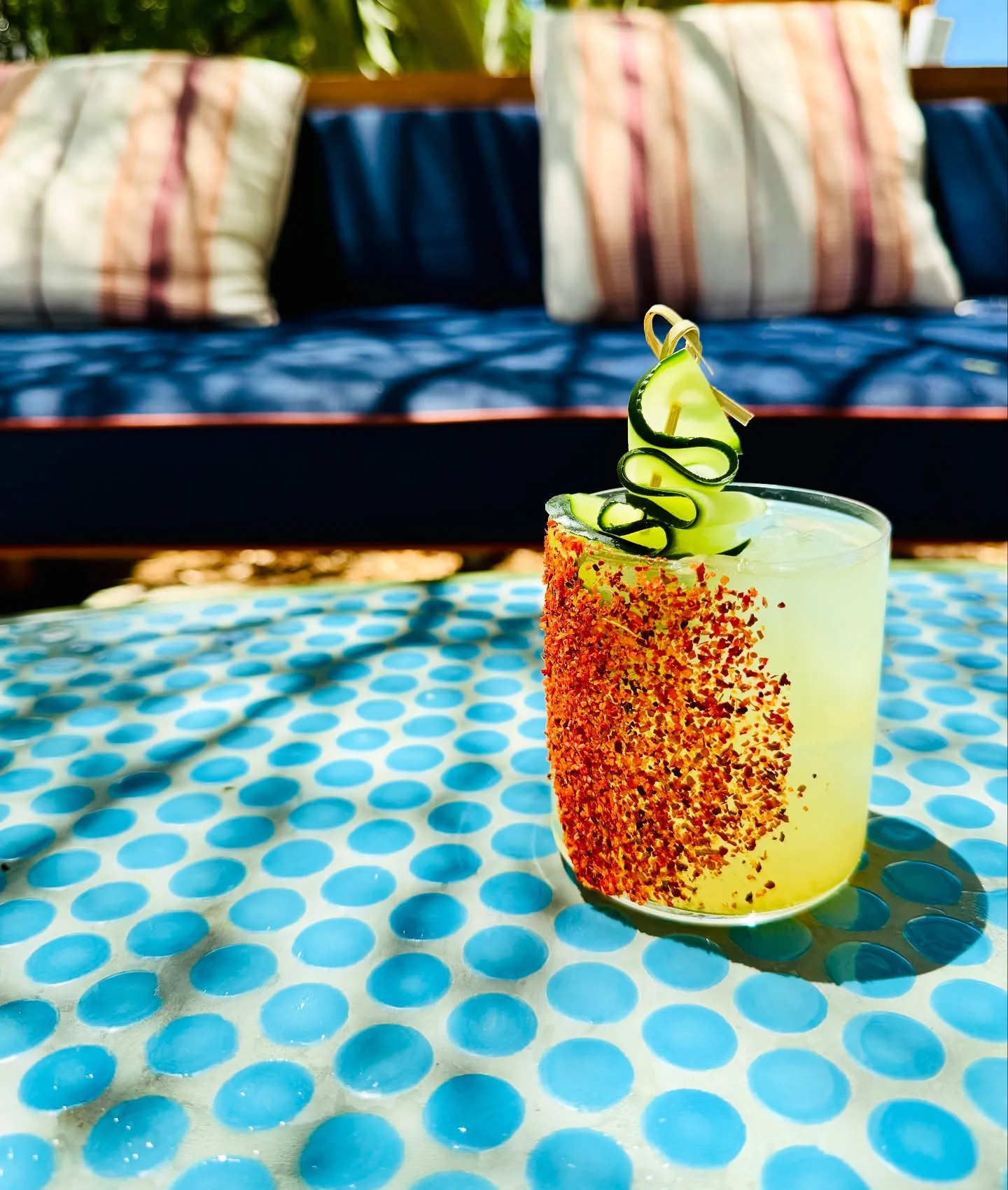 Bright yellow cocktail with a chili-salt rim and lime twist beside a Palm Springs pool