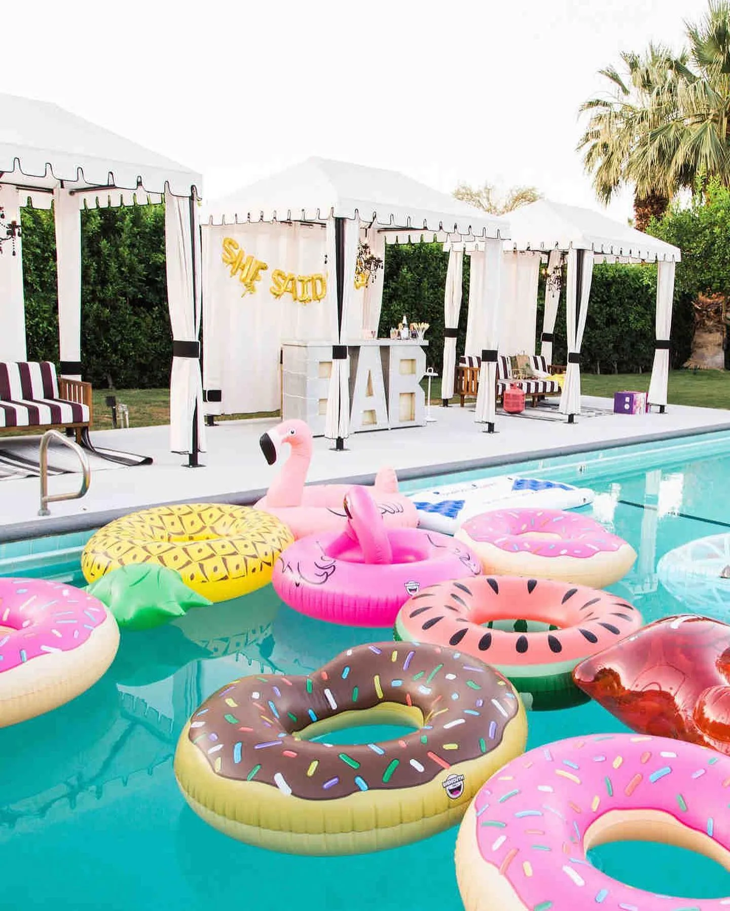 Palm Springs pool filled with colorful floats beside white cabanas and a cocktail bar