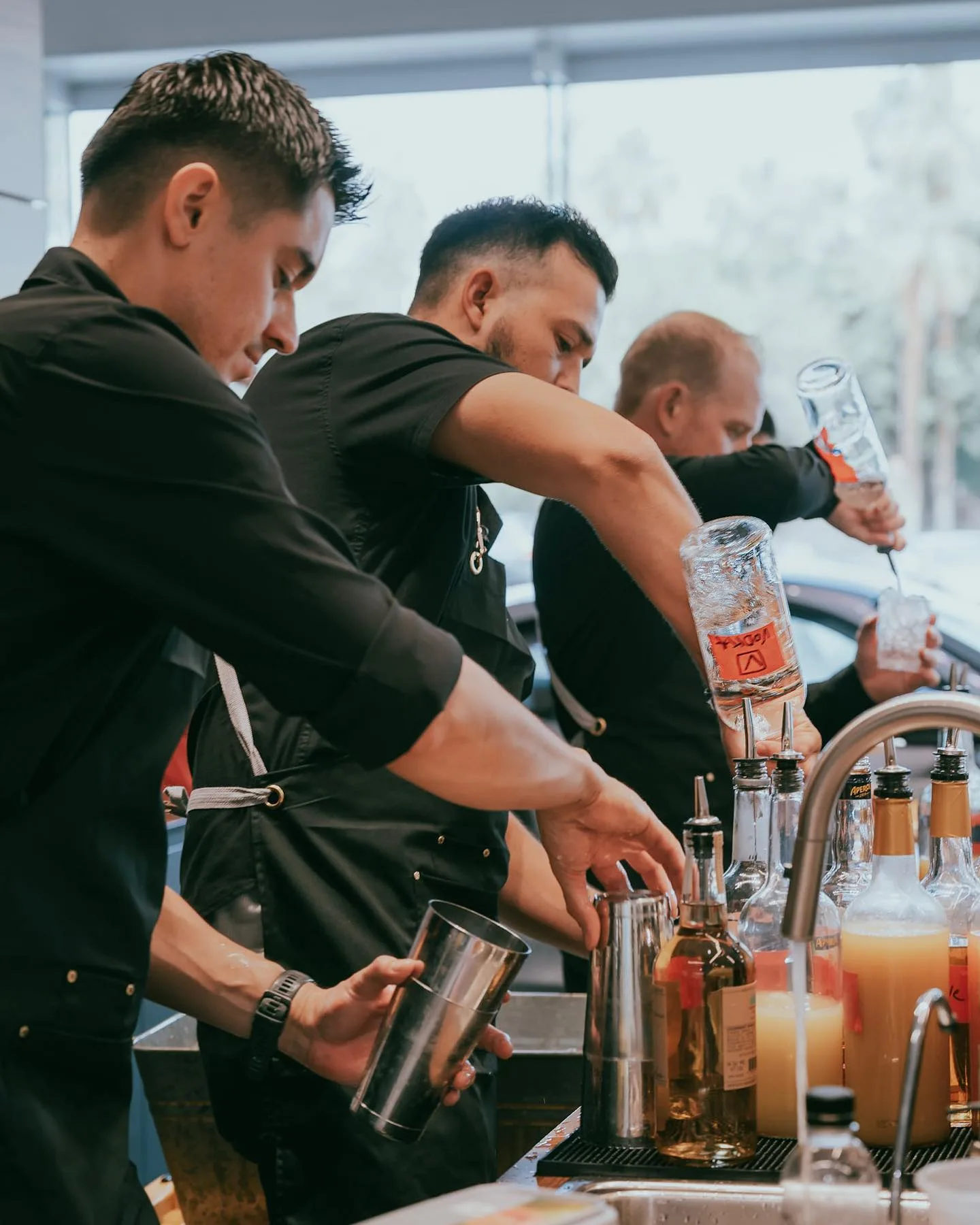 Three bartenders working shoulder to shoulder while pouring cocktails at a busy event bar