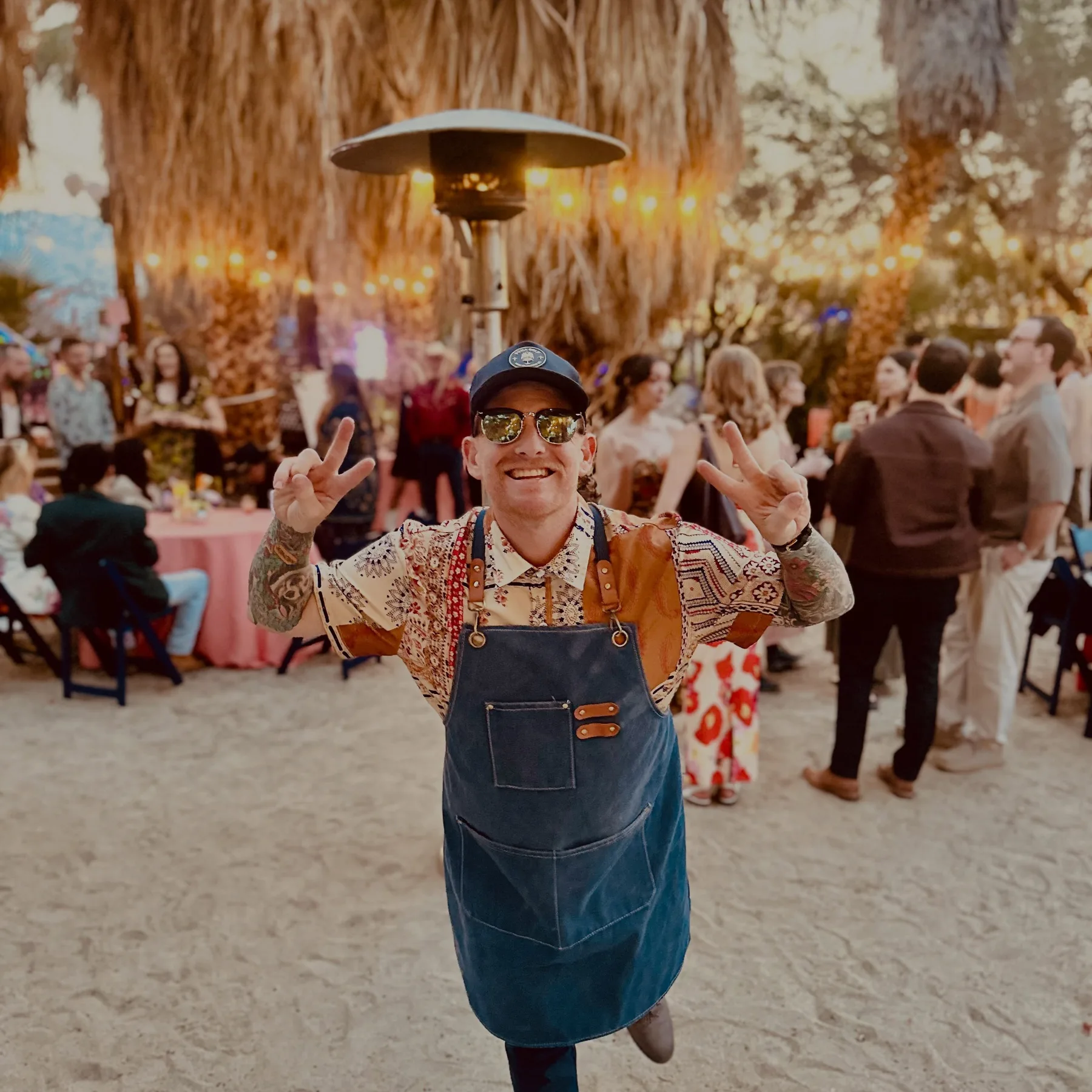 Bartender smiling and raising a cocktail shaker in front of a cheering outdoor wedding crowd