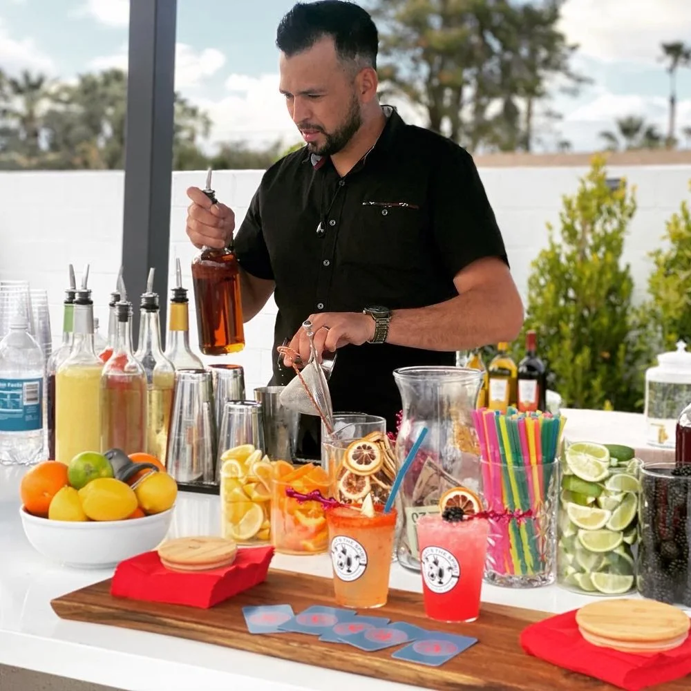 Bartender preparing drinks behind a colorful outdoor cocktail station
