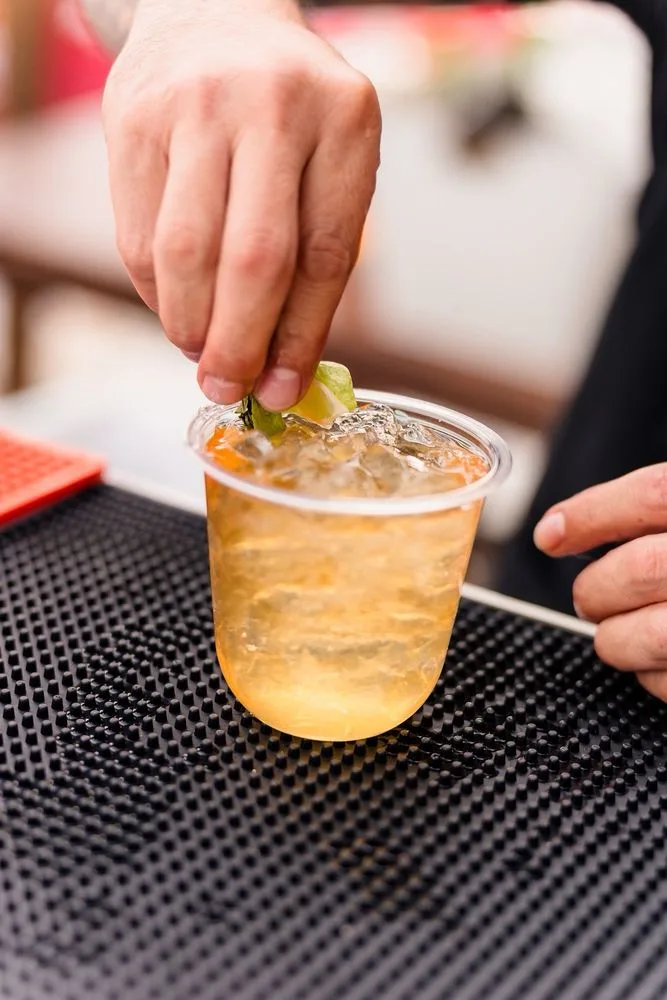 Bartender pressing a fresh lime garnish into an amber cocktail over ice