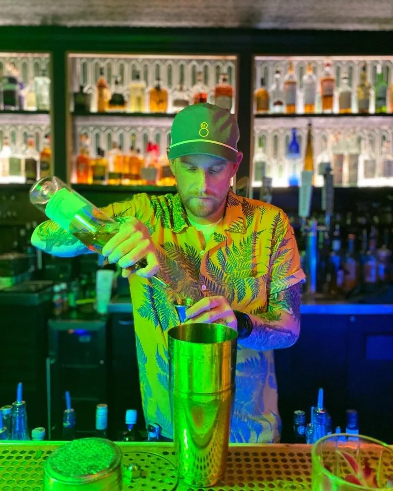 Bartender measuring a pour under vivid green and blue nightlife lighting