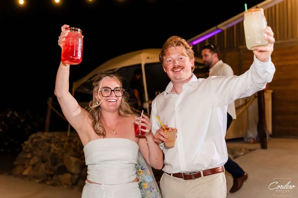 Newlyweds raising colorful cocktails together at their outdoor evening reception