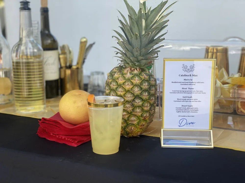 Wedding bar display with pineapple, fresh citrus, bottles, and a custom drink menu