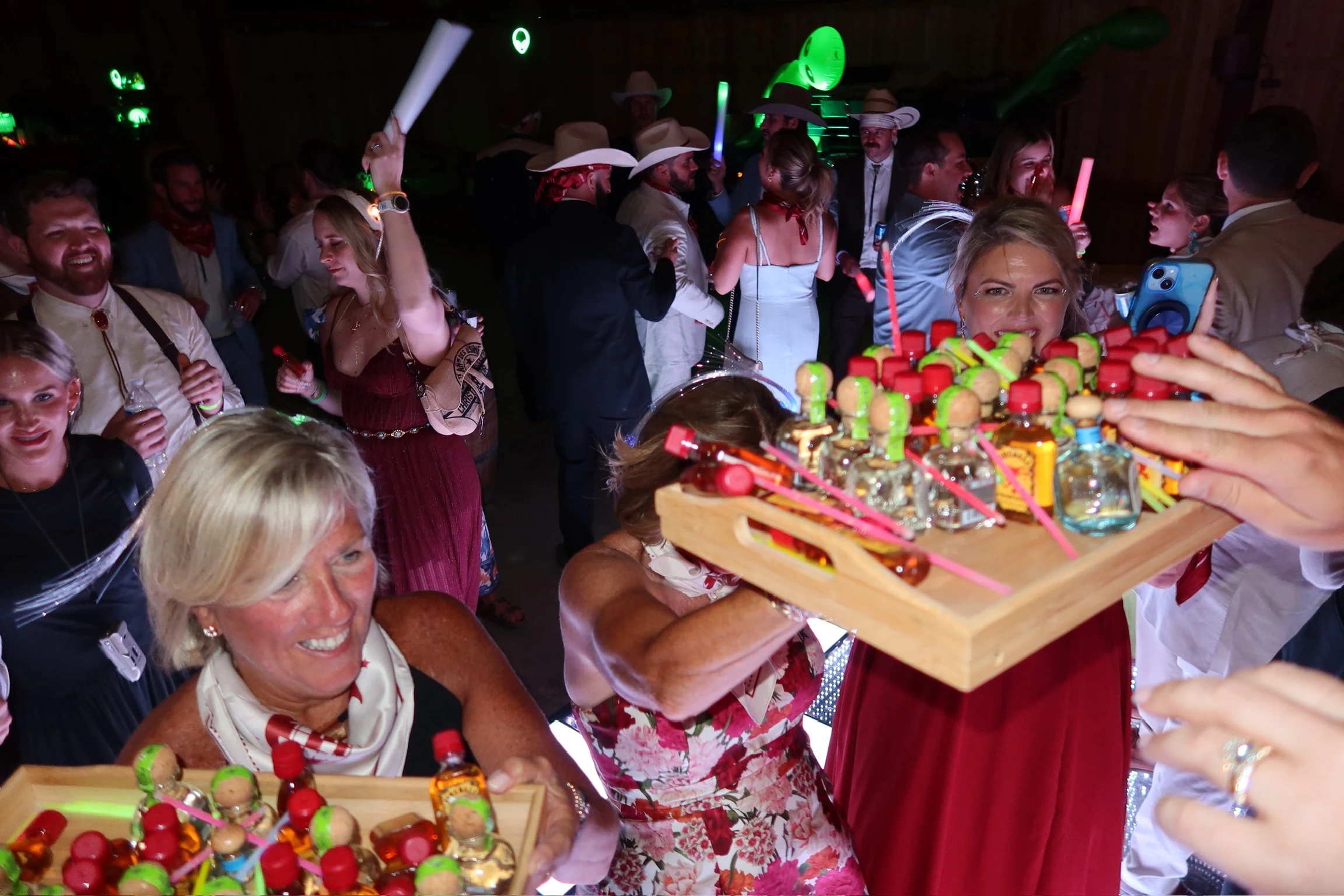 Guests celebrating on a crowded nighttime dance floor as trays of party shots arrive