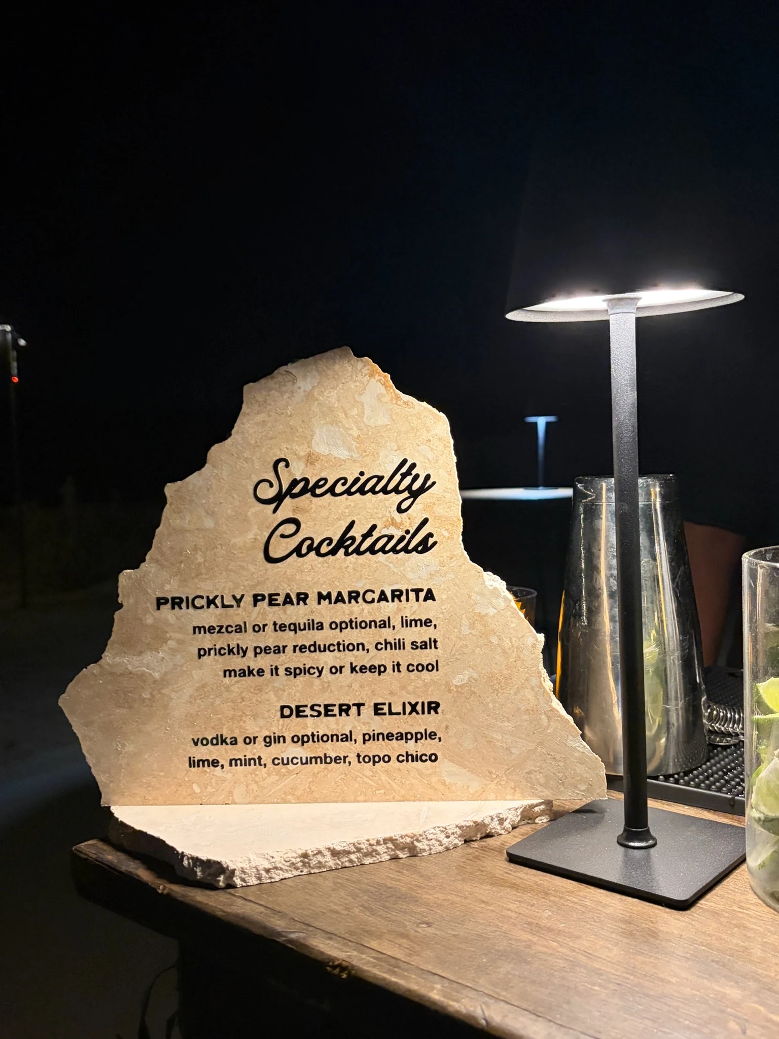 Stone-shaped specialty cocktail menu illuminated on a nighttime wedding bar