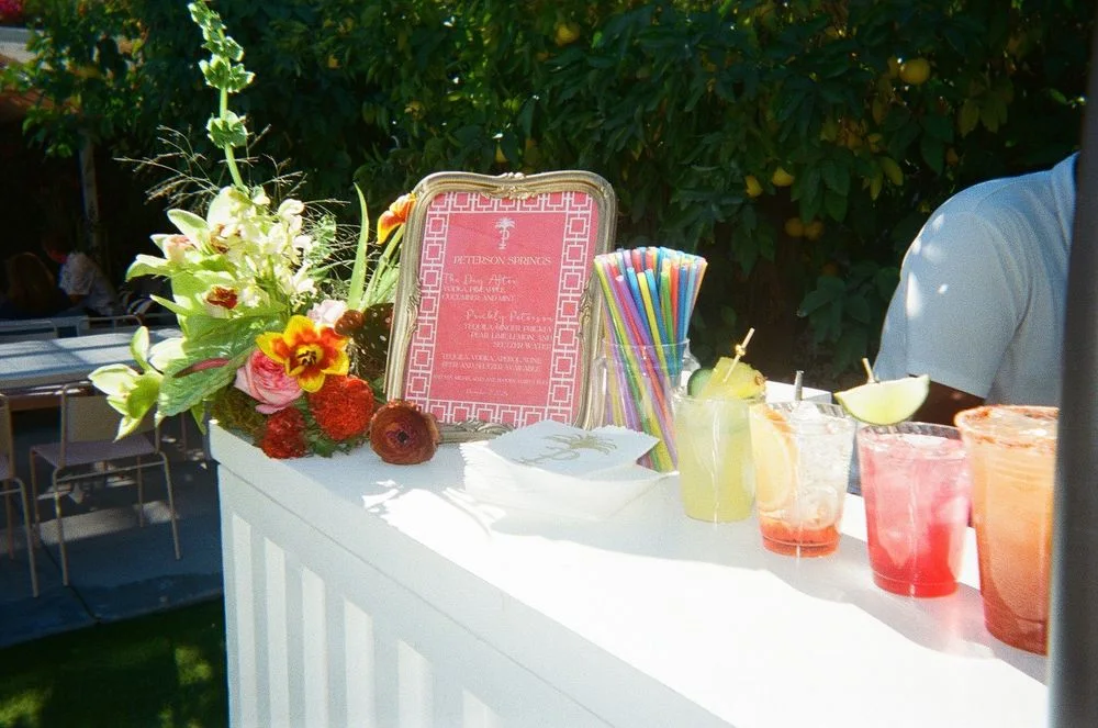 A white event bar decorated with flowers and colorful cocktails.